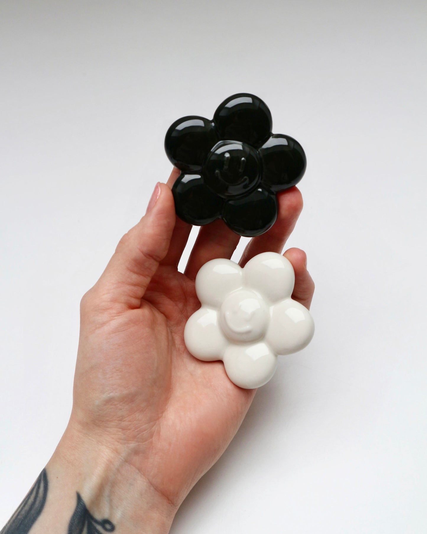 BUNBUN’S HAPPY FLOWER - collectible art toy sculpture. White and black flower-shaped figurines in front of a branded box. Hand holding a black and white ceramic flower-shaped object against a white background.