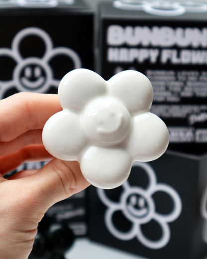 BUNBUN’S HAPPY FLOWER - collectible art toy sculpture. White flower-shaped figurine held by a hand with a black and white background featuring smiley face flower designs.